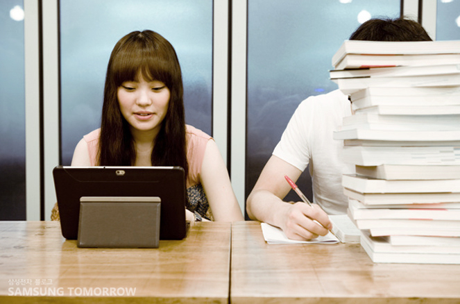 갤럭시 탭을 가진 여자와 책을 쌓아논 남자