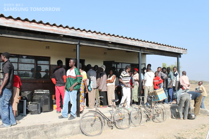 고장난 기계들을 가지고 줄을 선 사람들