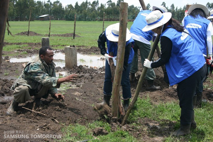 땅을 파고 나무를 세우는 자원봉사자들