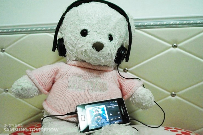 스마트폰에 연결된 헤드셋을 쓰고 있는 곰돌이 인형