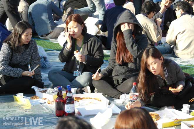 돗자리에 앉아 피자를 먹는 직원들