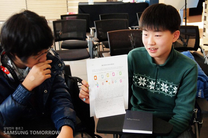 상상속의 휴대폰의 모습을 말하고 있는 초등학생의 모습