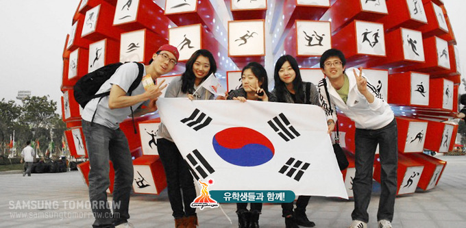 경기장 앞에서 유학생들과 함께 태극기 사진을 들고 사진을 찍은 스토리텔러들