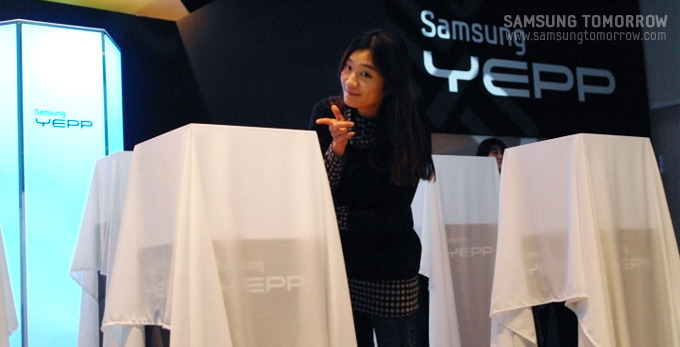 하얀천으로 덮어논 신제품앞에서 기념사진을 촬영하는 스토리텔러의 모습