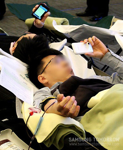 스마트 폰을 하며 헌혈을 하고 있는 삼성 직원들