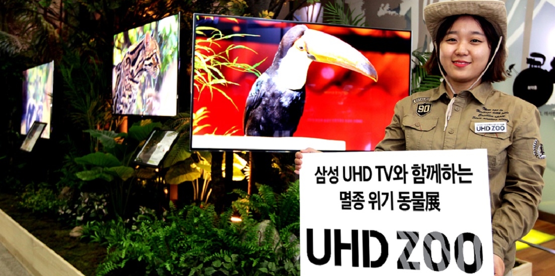 행사장 직원이 삼성 UHD TV와 함께하는 멸종위기 동물展 UHD ZOO 팻말을 들고 있습니다.