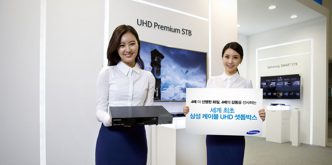 두 여성 모델이 UHD 셋톱박스와 4배 더 선명한 화질, 4배의 감동을 전하는 세계 최초 삼성 케이블 UHD 셋톱박스라고 쓰인 푯말을 들고 서 있습니다