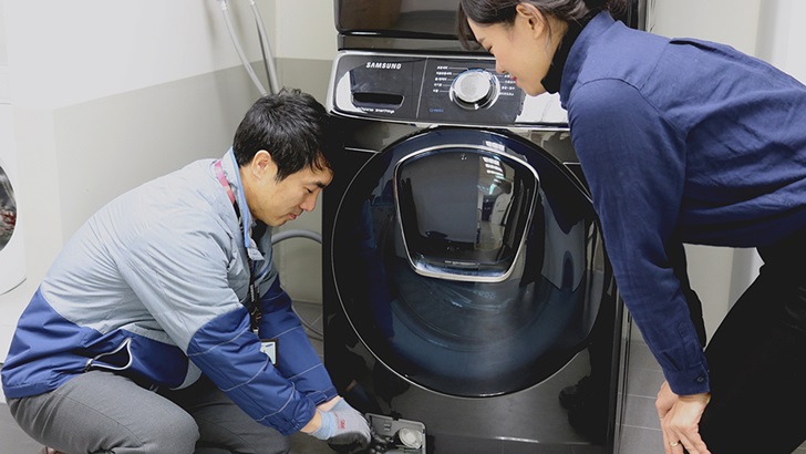 삼성전자서비스 수리 엔지니어가 출장 점검 서비스를 신청한 고객에게 플러스 원 케어 서비스의 일환으로 드럼세탁기 배수펌프 잔수 제거 방법을 설명하고 있는 모습