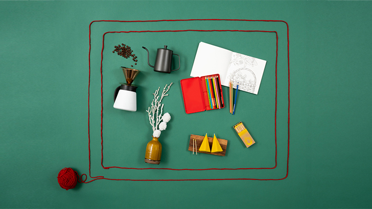 더 프레임 모양으로 만들어진 털실 안에 커피 드리퍼 세트, 컬러링 북과 색연필, 향초, 화병과 꽃이 있는 모습