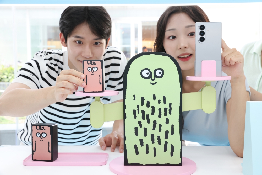 서울 코엑스 'The Galaxy UNFOLDERS' 체험존 방문객들이 아티스트 '장 줄리앙(Jean Jullien)'의 캐릭터를 활용한 무게 측정 키트로 '갤럭시 Z 폴드7'의 무게를 재는 모습